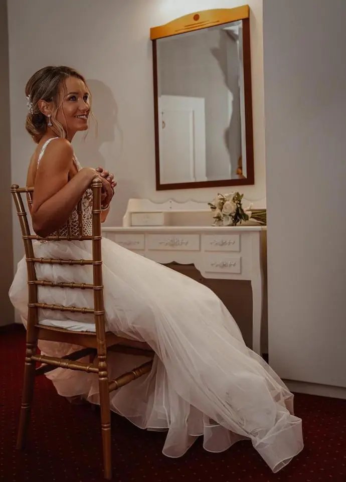 Das Mädchen in ihrem Brautkleid sitzt auf einem Stuhl und posiert mit ihrer Hochzeitsfrisu